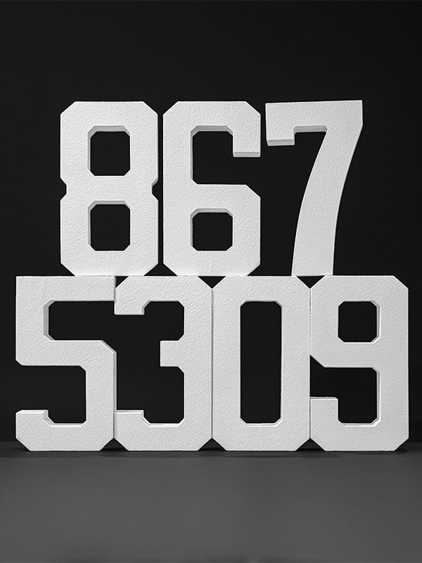 White hard-coated foam stand-alone number props arranged as 867 over 5309 on a dark studio background.