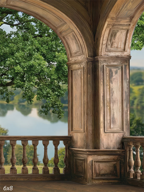 This photography backdrop shows a stone archway terrace with a column and balustrade overlooking a river and countryside landscape. The studio background frames a portrait subject with architectural depth and natural scenery.