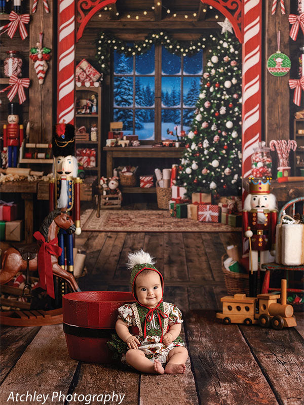 Sugar Workshop Santa's workshop interior photography backdrop shown with a baby in a gingerbread-print outfit seated by a red bucket on the floor CP-8910