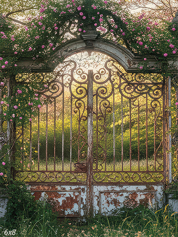 A wrought-iron garden gate draped in pink roses glows in the golden light of sunset, framed by vines and aged stone.