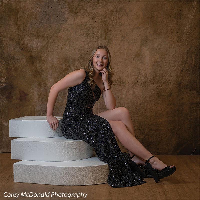Textured Gold Radiance printed photography backdrop shown in a styled studio session with a senior in a black sequin gown seated on white posing steps with a hand near her chin OM-2606