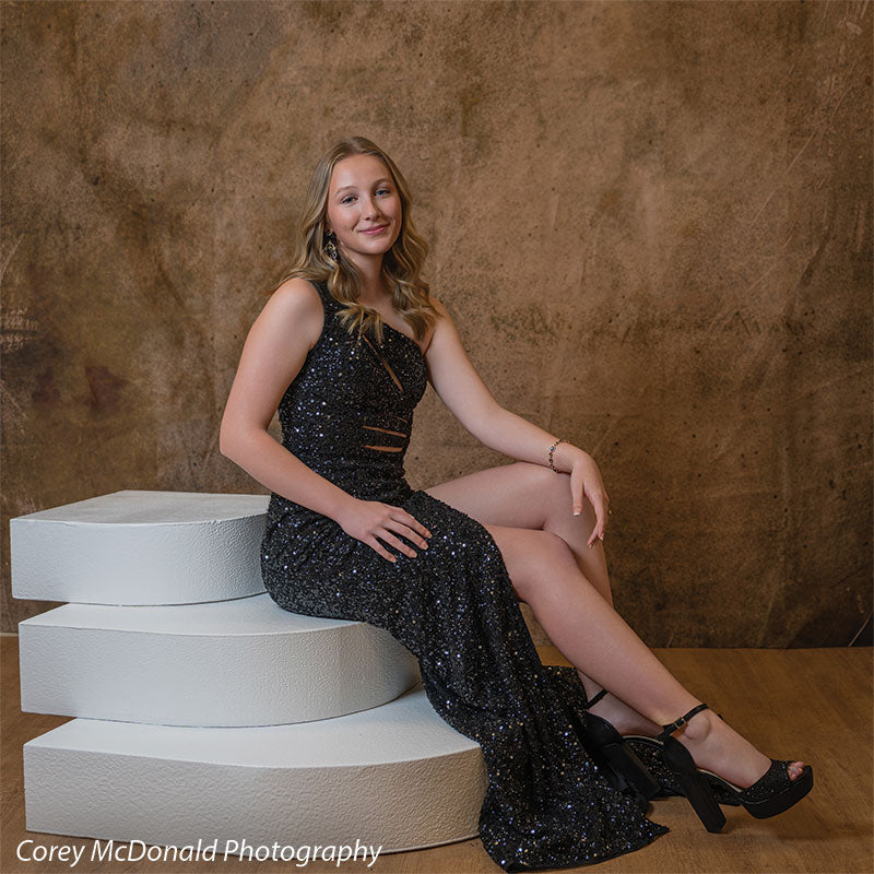 Textured Gold Radiance printed photography backdrop shown in a styled studio session with a senior in a black sequin gown seated on stacked round white posing steps and smiling OM-2606