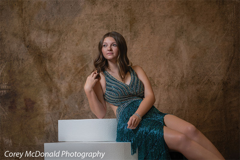 Textured Gold Radiance printed photography backdrop shown in a styled studio session with a senior in a teal fringed gown seated on stacked white posing steps looking to the side OM-2606