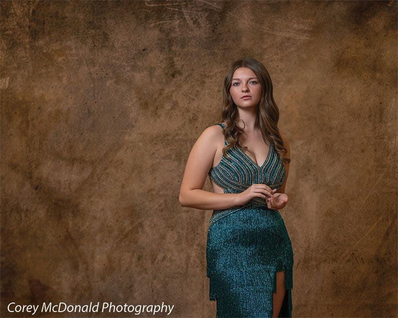 Textured Gold Radiance printed photography backdrop shown in a styled studio session with a senior in a teal fringed gown standing full-length in a wide studio view OM-2606