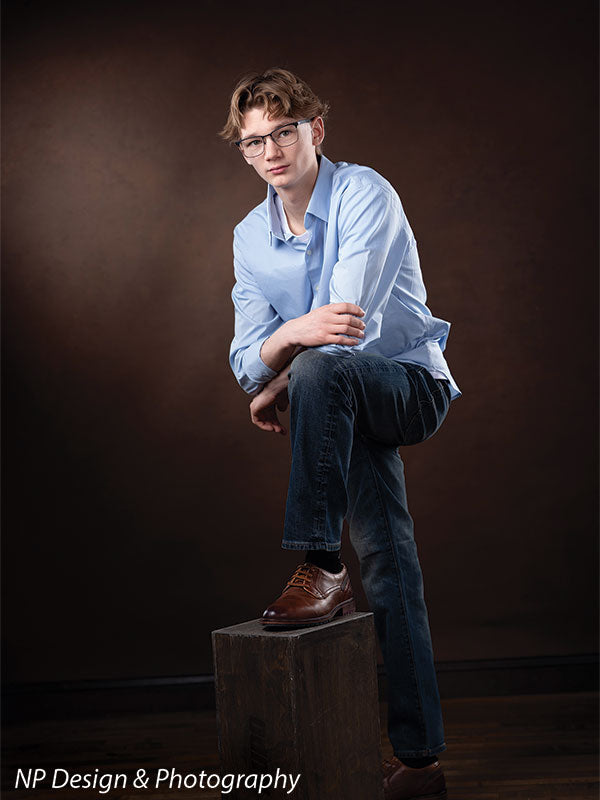 Toasted chestnut old masters photography backdrop shown with a senior boy in a light blue shirt with one foot up on a box in a three-quarter pose OM-2622