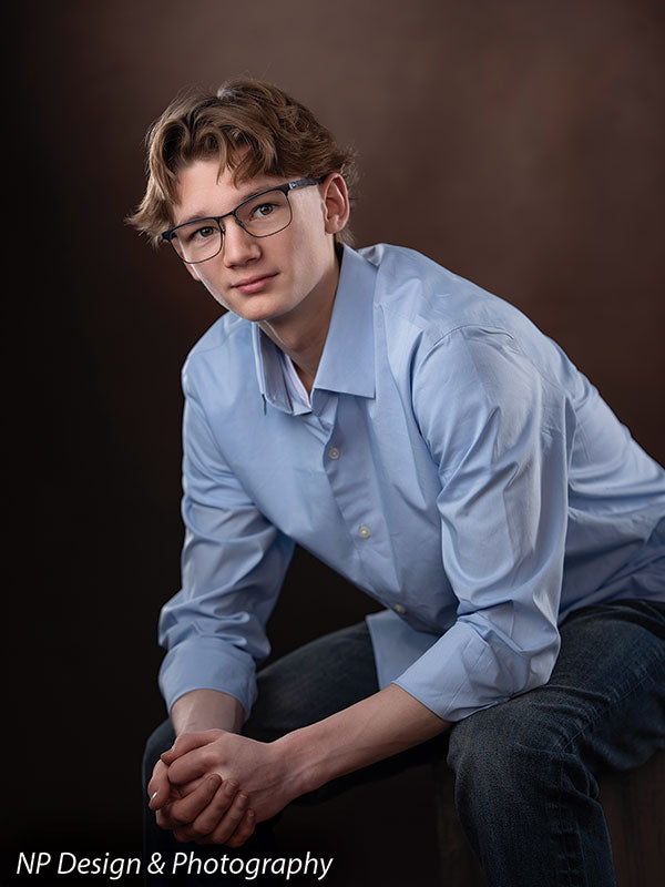 Toasted chestnut old masters photography backdrop shown with a senior boy in a light blue shirt seated with clasped hands in a close pose OM-2622