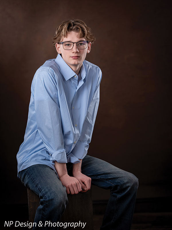 Toasted chestnut old masters photography backdrop shown with a senior boy in a light blue shirt seated on a box in a calm pose OM-2622
