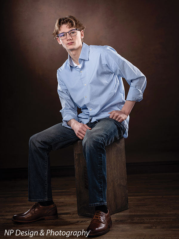 Toasted chestnut old masters photography backdrop shown with a senior boy in a light blue shirt seated on a box with a hand on his hip OM-2622