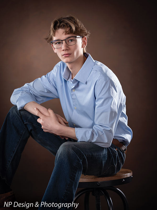 Toasted chestnut old masters photography backdrop shown with a senior boy in a light blue shirt seated on a stool with his forearm on his knee OM-2622