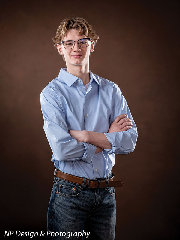 Toasted chestnut old masters photography backdrop shown with a senior boy in a light blue shirt standing with his arms crossed, smiling OM-2622
