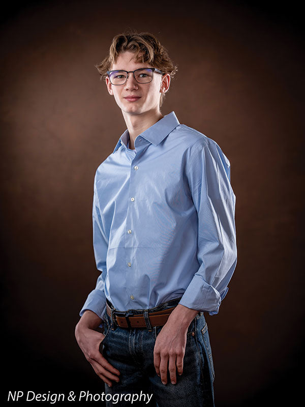 Toasted chestnut old masters photography backdrop shown with a senior boy in a light blue shirt standing in a three-quarter pose, smiling OM-2622