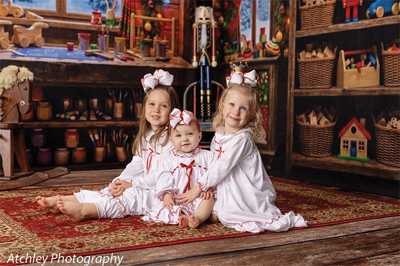 Toy Maker Santa's workshop craft-table photography backdrop shown as part of a Santa's workshop Christmas corner set with three young girls in white Christmas nightgowns seated on the workshop rug CP-8943