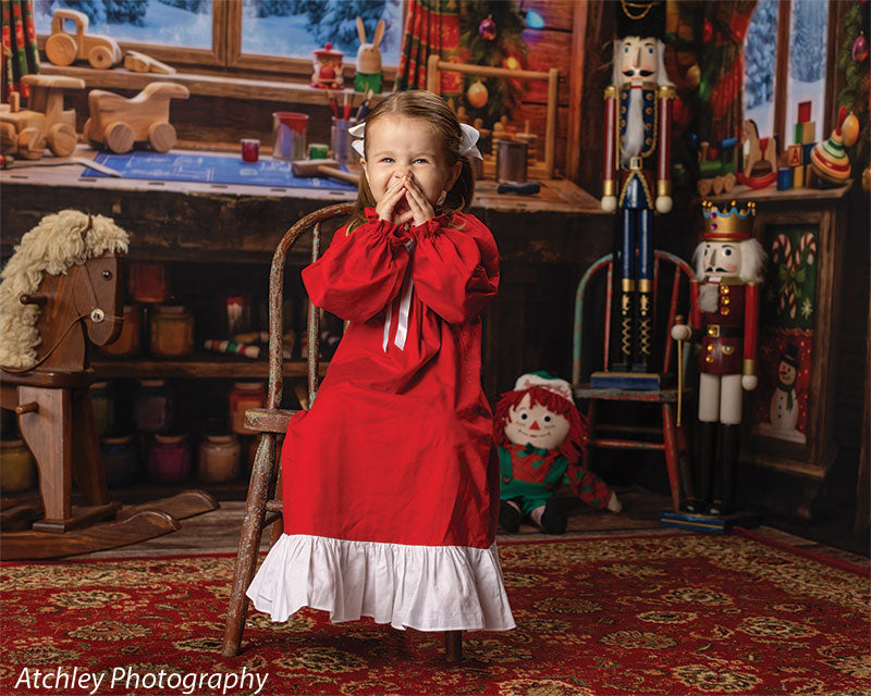 Toy Maker Santa's workshop craft-table photography backdrop shown as part of a Santa's workshop Christmas corner set with a young girl in a red Christmas gown giggling with hands near her face CP-8943
