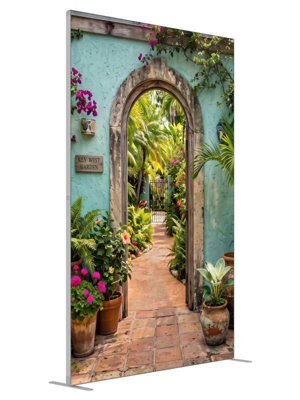 A turquoise stucco courtyard wall with a stone archway opening onto a lush tropical garden, 5ft photography backdrop panel for Denny StudioEdge silicone edge frame, angled view