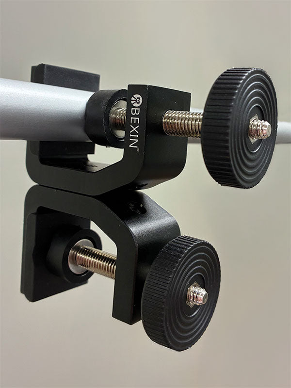 Black metal Twist Flex Clamp gripping a round crossbar at an angle, showing its stacked double-clamp design and knurled thumb knobs