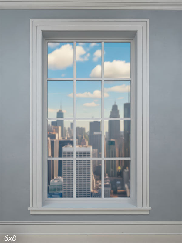 Studio backdrop showing a close-up view of a white-trimmed window set into a cool gray wall, looking out onto a softly blurred city skyline under a bright blue sky with clouds.