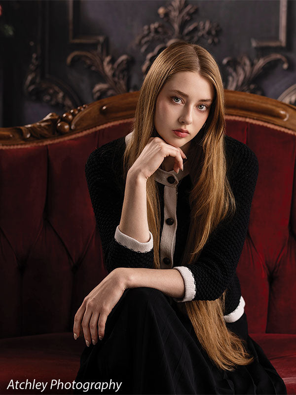 Velvet Swag ornate gray paneled wall with red velvet draping photography backdrop shown with a senior girl seated on the red velvet sofa in a thoughtful pose CP-8899