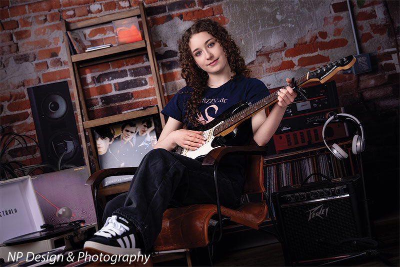 Vintage exposed brick music studio photography backdrop shown with a senior girl seated holding an electric guitar in a relaxed pose CP-8630