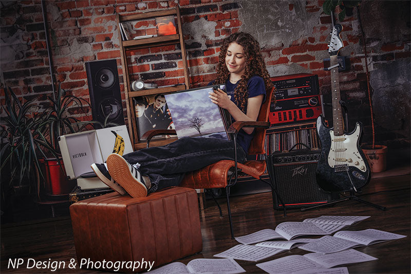 Vintage exposed brick music studio photography backdrop shown with a senior girl reclining in a leather chair holding a framed album print CP-8630