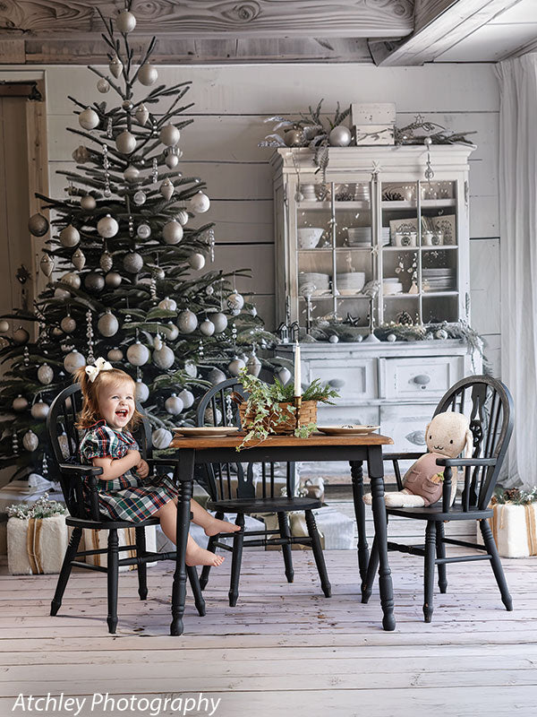 Farmhouse Christmas backdrop with decorated tree, white hutch, holiday gifts, and rustic dining table, featuring a young girl laughing in a plaid dress, perfect for cozy seasonal photo sessions.