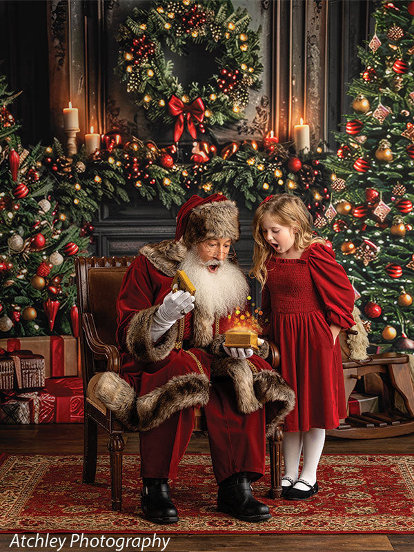Santa Claus holding a glowing gift box while a surprised young girl in a red dress stands beside him, in front of a warm Christmas living room backdrop featuring a decorated tree, wreath, garland, candles, wrapped gifts, and a lit fireplace.