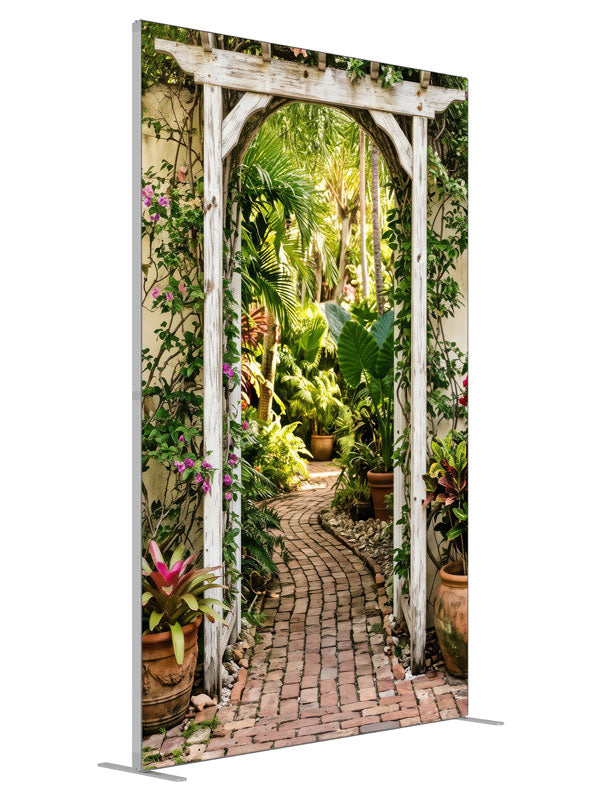 A whitewashed wood arbor in a cream wall opening onto a lush tropical garden with a brick path, 5ft photography backdrop panel for Denny StudioEdge silicone edge frame, angled view