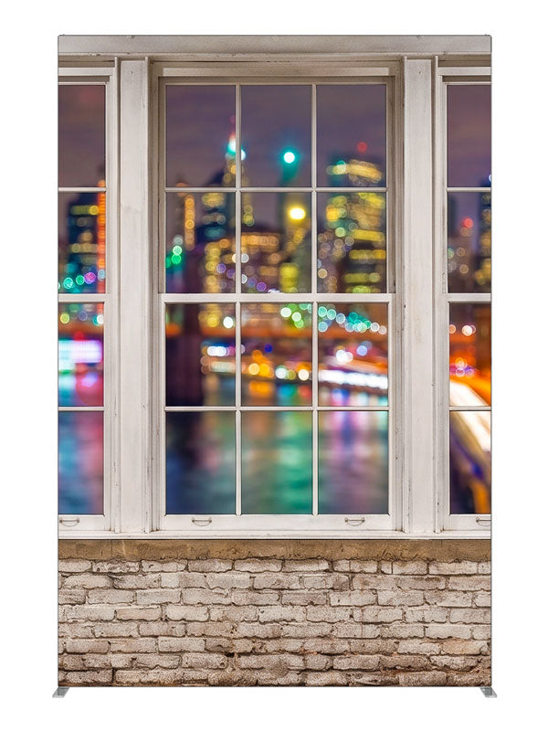 A whitewashed-brick loft with white-framed windows over a colorful bokeh city skyline at night, 5ft photography backdrop panel for Denny StudioEdge silicone edge frame
