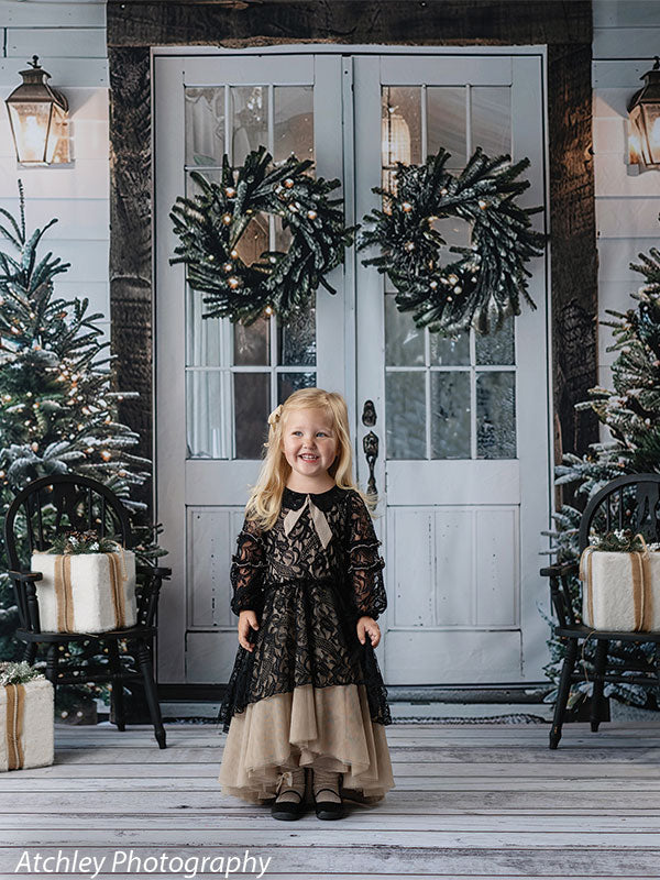 White French doors and Christmas trees backdrop with festive wreaths and wrapped presents, featuring a young girl in a black and gold dress, ideal for elegant holiday portraits.