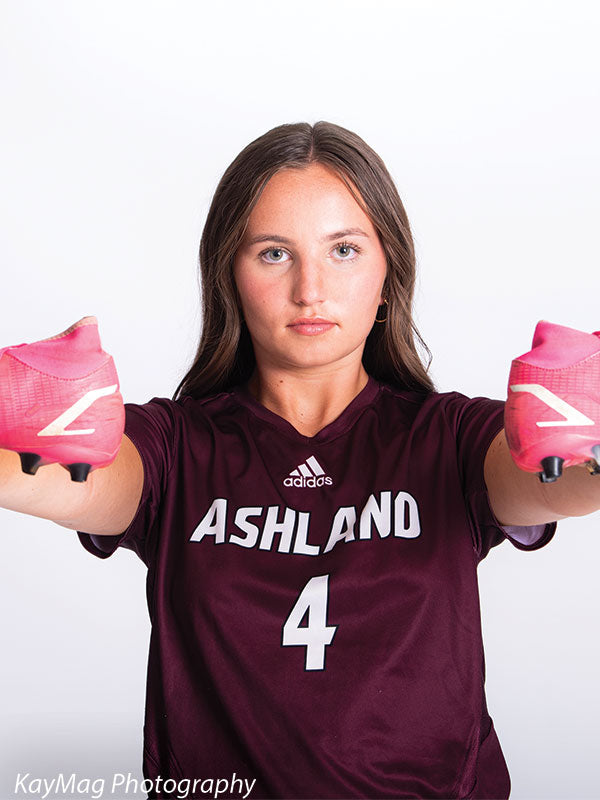 Intense close-up of female soccer player in maroon jersey holding cleats, captured on a clean white sports photography background.