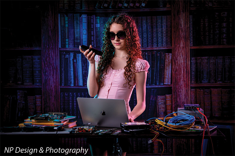 Worn volumes book shelf photography backdrop shown with a senior girl wearing sunglasses holding a small device above her laptop CP-7317