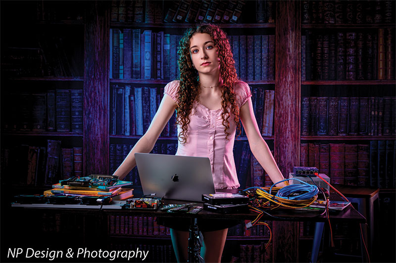Worn volumes book shelf photography backdrop shown with a senior girl standing behind a desk with a laptop and tangled cables CP-7317