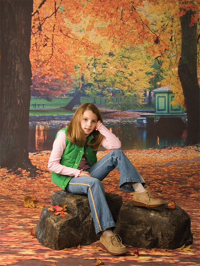 Leaf-strewn ground beneath arching fall foliage near tranquil water.