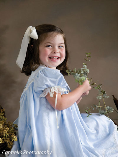 Smiling girl holds greenery against a painterly brown floral backdrop, evoking a soft botanical setting—suited for children’s portraits and traditional family sessions.
