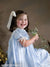 Smiling girl holds greenery against a painterly brown floral backdrop, evoking a soft botanical setting—suited for children’s portraits and traditional family sessions.