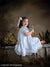 Girl in heirloom blue dress sits on stone ledge in front of a hand-painted floral garden backdrop—ideal for storytelling-style children’s photography and family scenes.