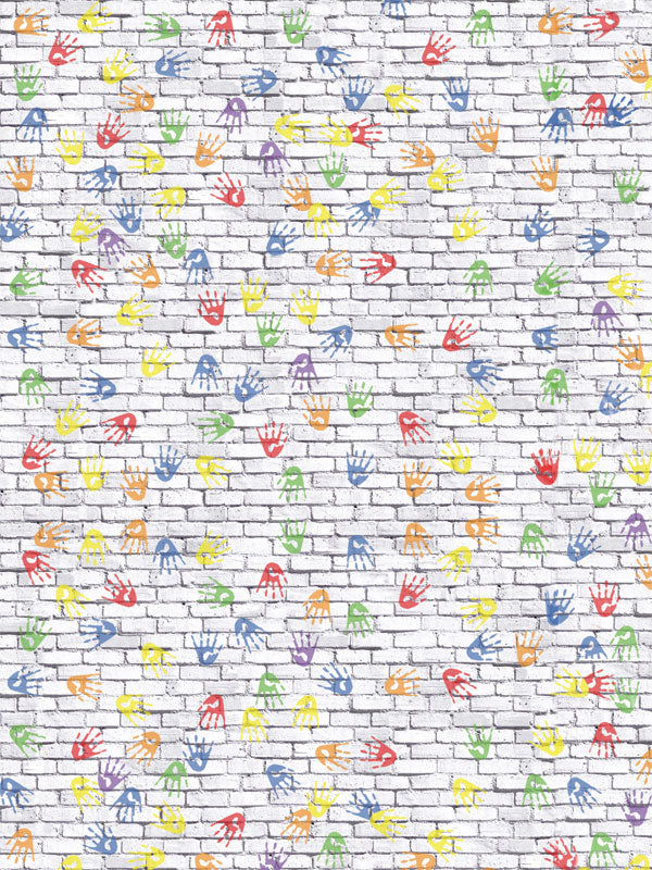 A bright kids photography backdrop featuring a white brick wall with multicolored painted handprints scattered across the surface.