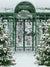 Enchanted Winter Garden Photography Backdrop - Photography backdrop featuring a serene winter garden with a green wrought-iron gate, two snow-covered Christmas trees, and fresh snow.