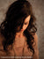 Female model with dark hair poses under warm lighting in front of a soft beige European tile backdrop—perfect for senior portraits and stylized studio photography.