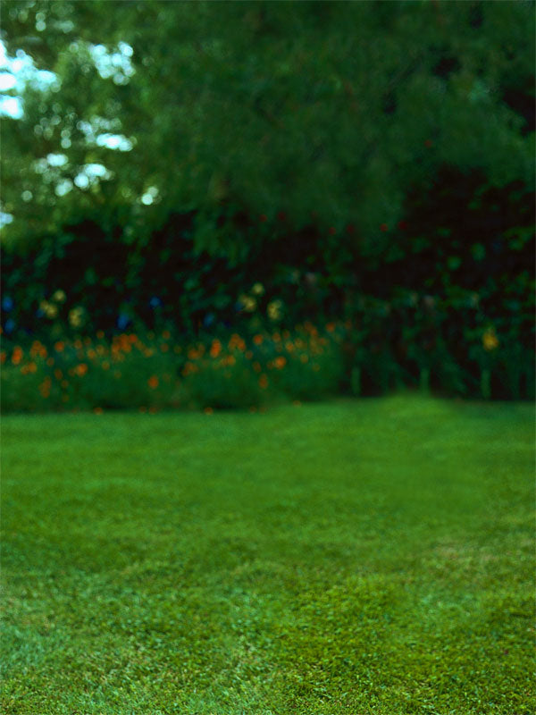 A lush green lawn photography backdrop with softly shaded foliage and scattered orange wildflowers along a hedgerow.