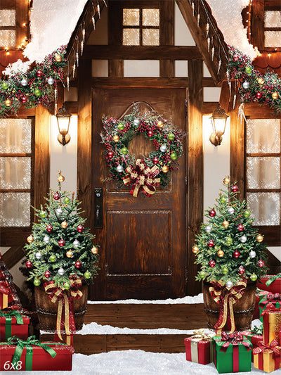 Festive Christmas Porch Photography Backdrop - Photography backdrop featuring a cozy Christmas porch with a decorated rustic wooden door, festive wreath, Christmas trees, and gift boxes.