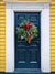 Festive Holiday Door Photography Backdrop - Festive black door with a holiday wreath set against a bright yellow exterior, perfect for Christmas photography backdrops.