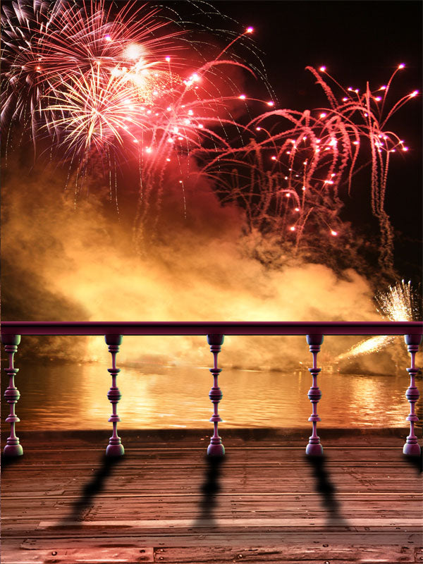 A high-impact photography backdrop with red fireworks bursting over a lake, viewed from a wooden deck with silhouetted railing.
