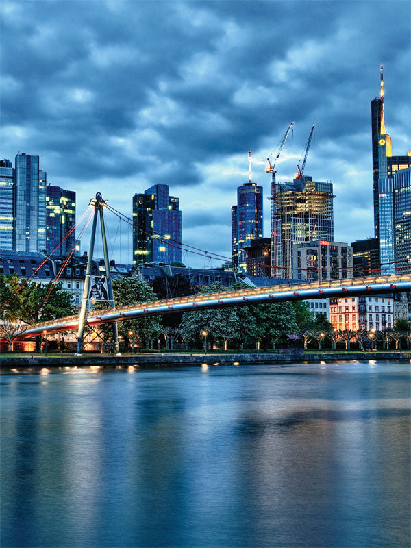 Frankfurt City Skyline Photography Backdrop - Frankfurt skyline during early evening with illuminated buildings reflecting on the river, featuring a sleek pedestrian bridge.