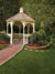 Elegant white gazebo surrounded by colorful flowers and a curved brick path.