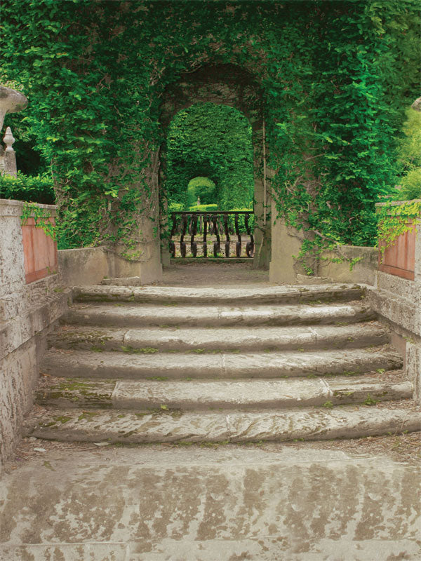 A romantic photography backdrop featuring weathered stone stairs leading to an ivy-covered archway and lush green garden.