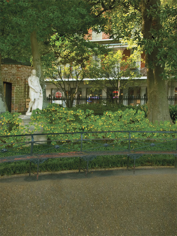 A garden photography backdrop featuring a classical white marble statue under a tree near a brick structure.