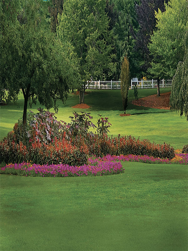 Manicured green lawn with vibrant flower beds and tree-lined background.