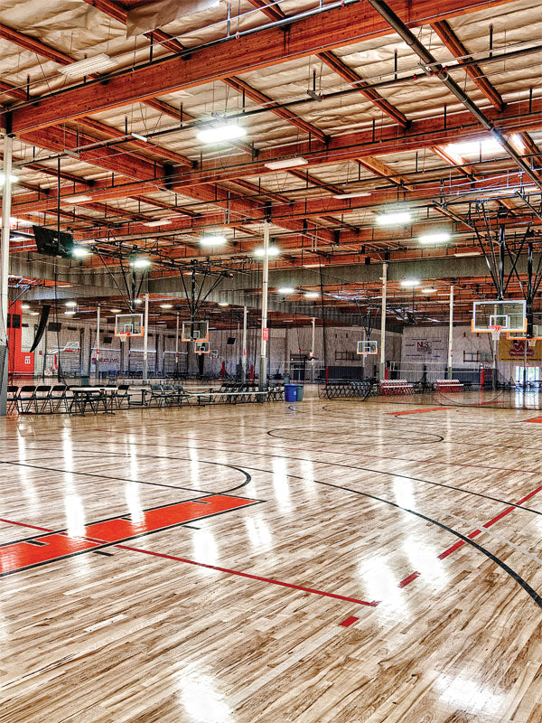 Indoor Basketball Court Backdrop - Spacious indoor basketball gym with polished wooden floors, multiple hoops, and industrial lighting.