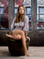 Casual seated pose with barefoot styling in front of red brick building and vintage loft windows—great for portrait sessions with a modern urban vibe.