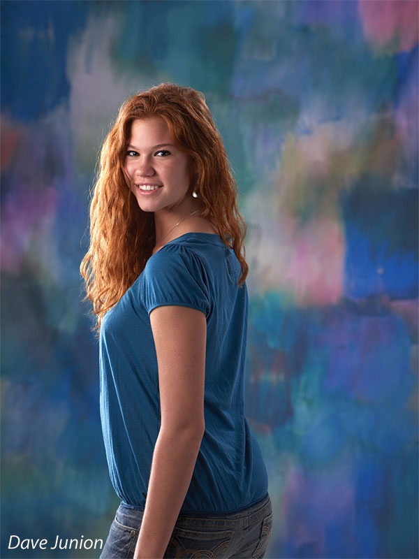 Studio backdrop with deep emerald, plum, and sapphire hues in soft painterly strokes.